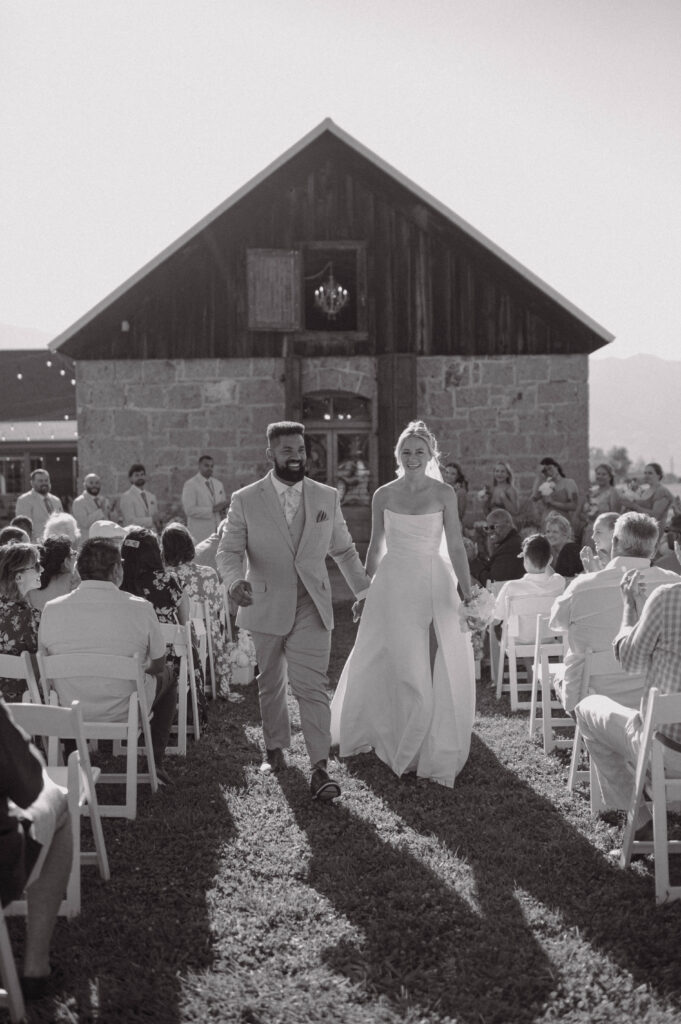 Black and white photo of the newlyweds walking back down the aisle after their Gansberg Ranch wedding ceremony.
