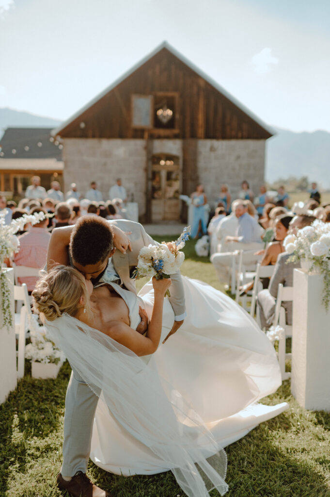 Groom dipping and kissing the bride in the ceremony aisle with the Stone Barn behind them.
