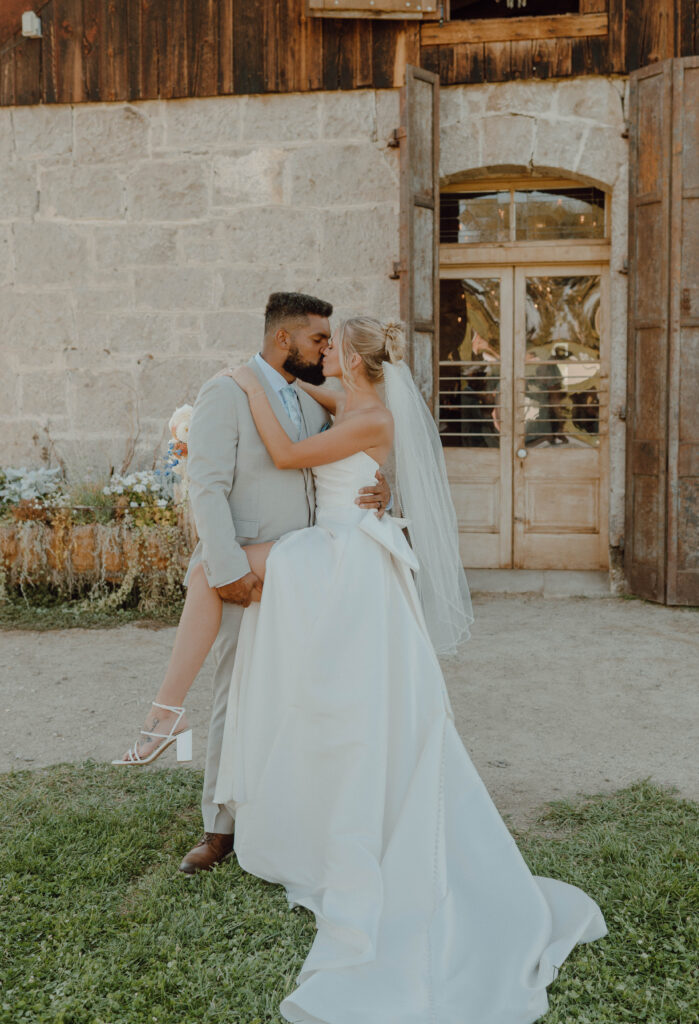 Newlyweds kissing outside the stone barn after their wedding ceremony.