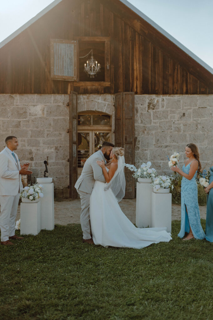 Bride and groom kissing during their golden hour wedding ceremony in front of the Stone Barn at Gansberg Ranch.