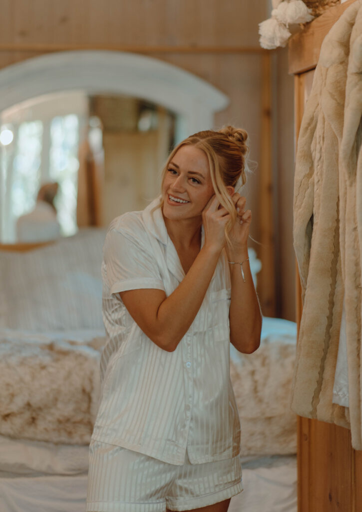 Bride putting on earrings while getting ready indoors.