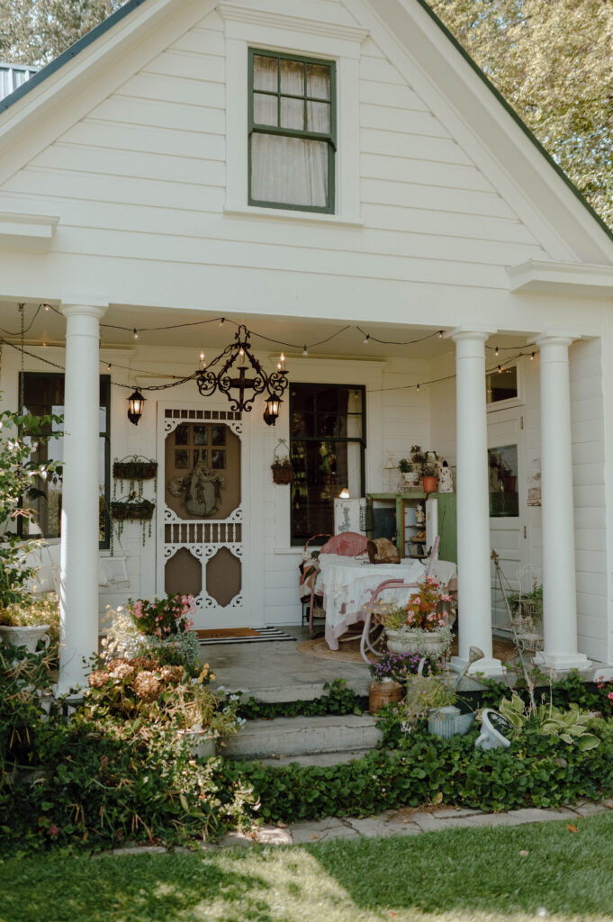Gansberg Ranch exterior farmhouse with a covered porch, flowers and garden greenery.