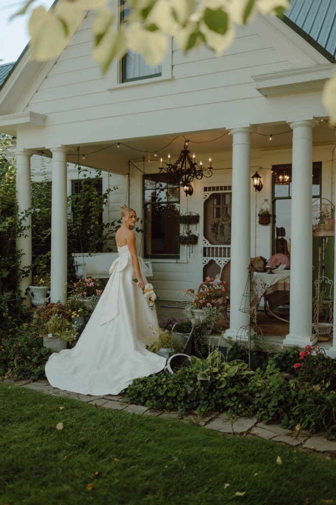 Bride holding her bouquet beside the flower-filled porch of the Gansberg Ranch house.