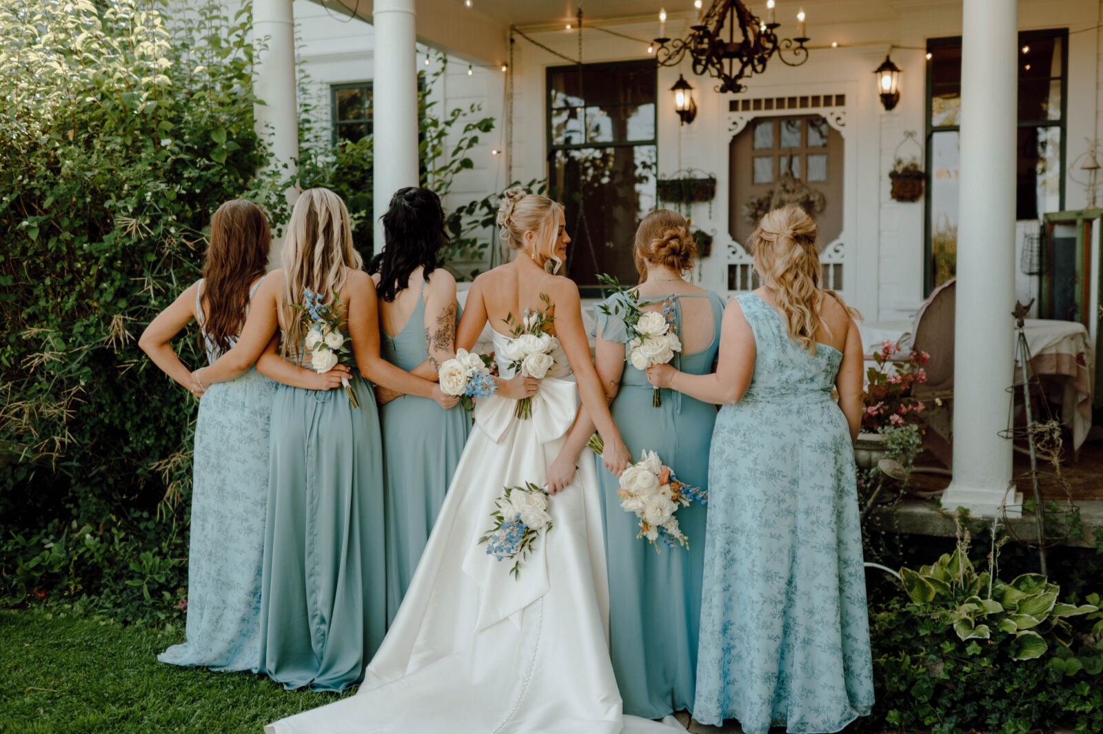 Bride and bridesmaids photographed from behind in blue dresses outside the Gansberg Ranch house.