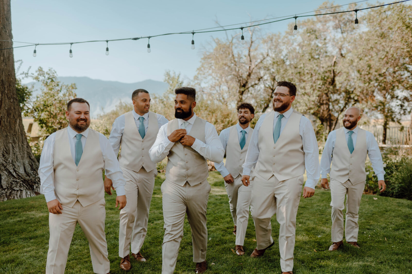 Groom and groomsmen walking together across the lawn beneath string lights from a Gansberg Rnach wedding.
