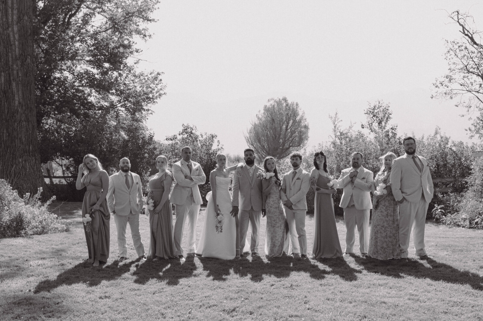 Black and white wedding party portrait outdoors with bridesmaids and groomsmen lined up together.