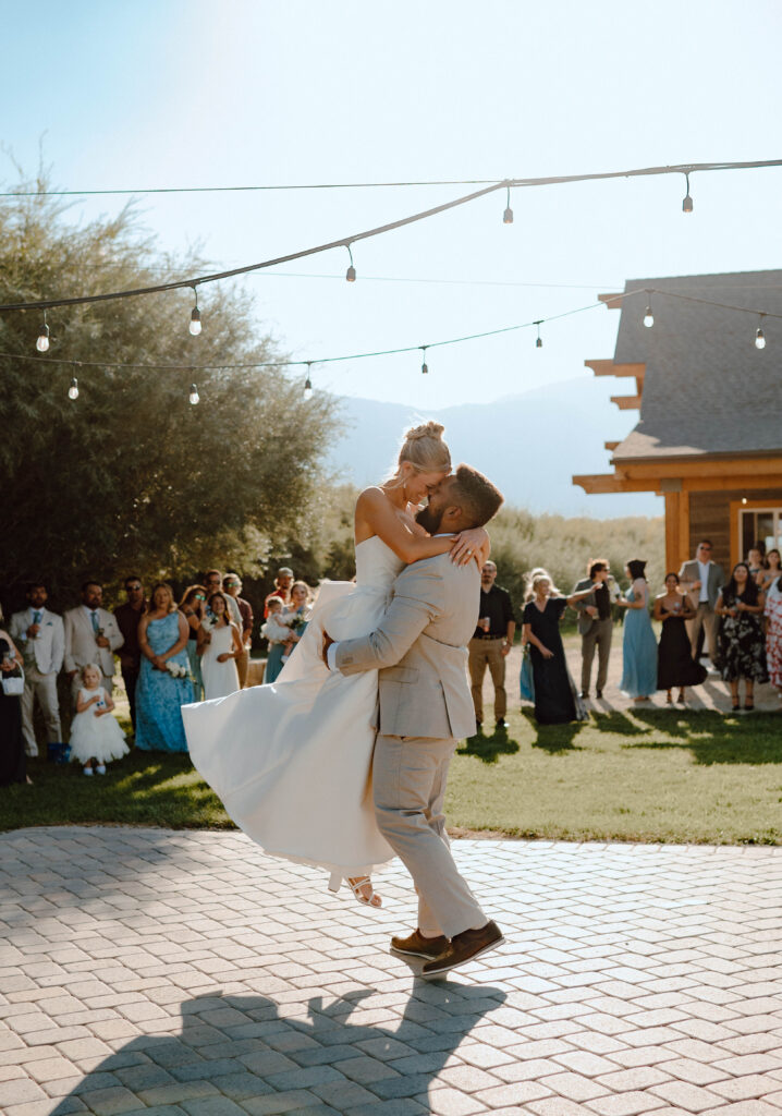 Groom lifting the bride during their first dance outdoors beneath string lights.