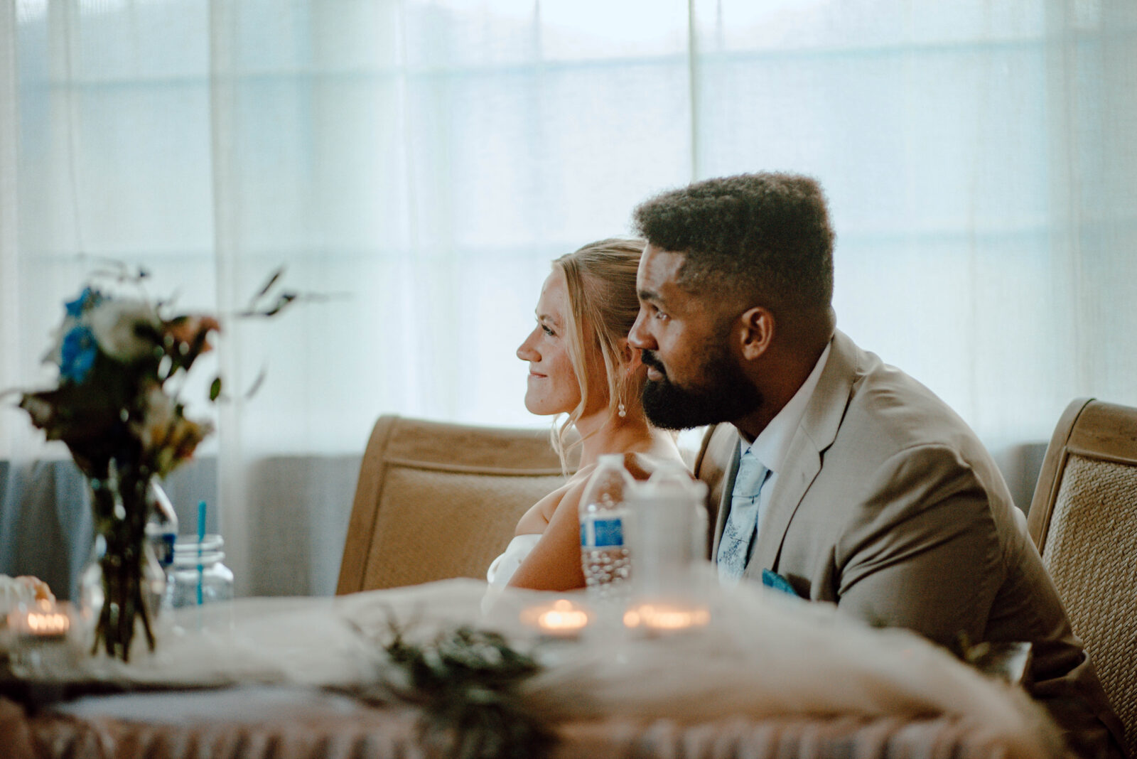 Bride and groom smiling as they listen to speeches.