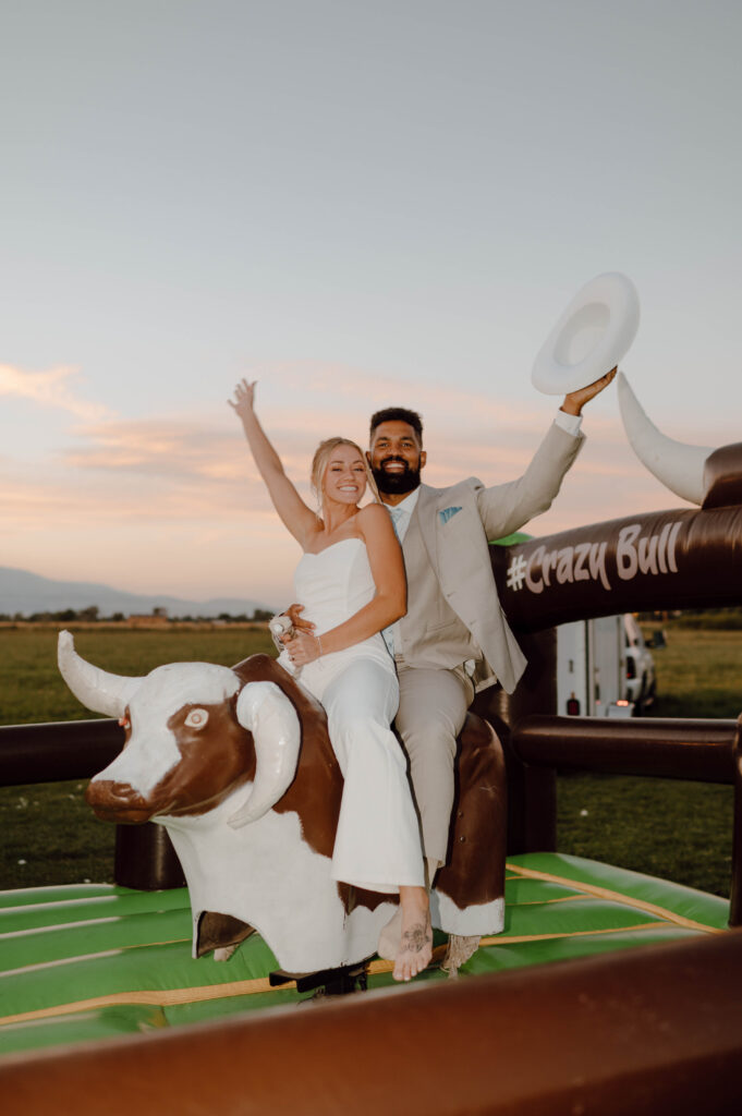 Bride and groom posing on a mechanical bull during their Gansberg Ranch wedding reception.