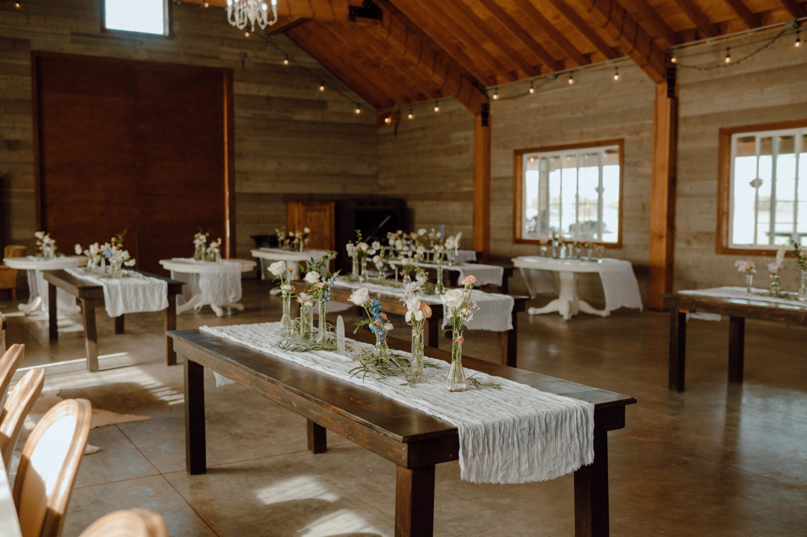 Gansberg Ranch Haybarn wedding reception setup with wooden farm tables, white runners and bud vase florals.
