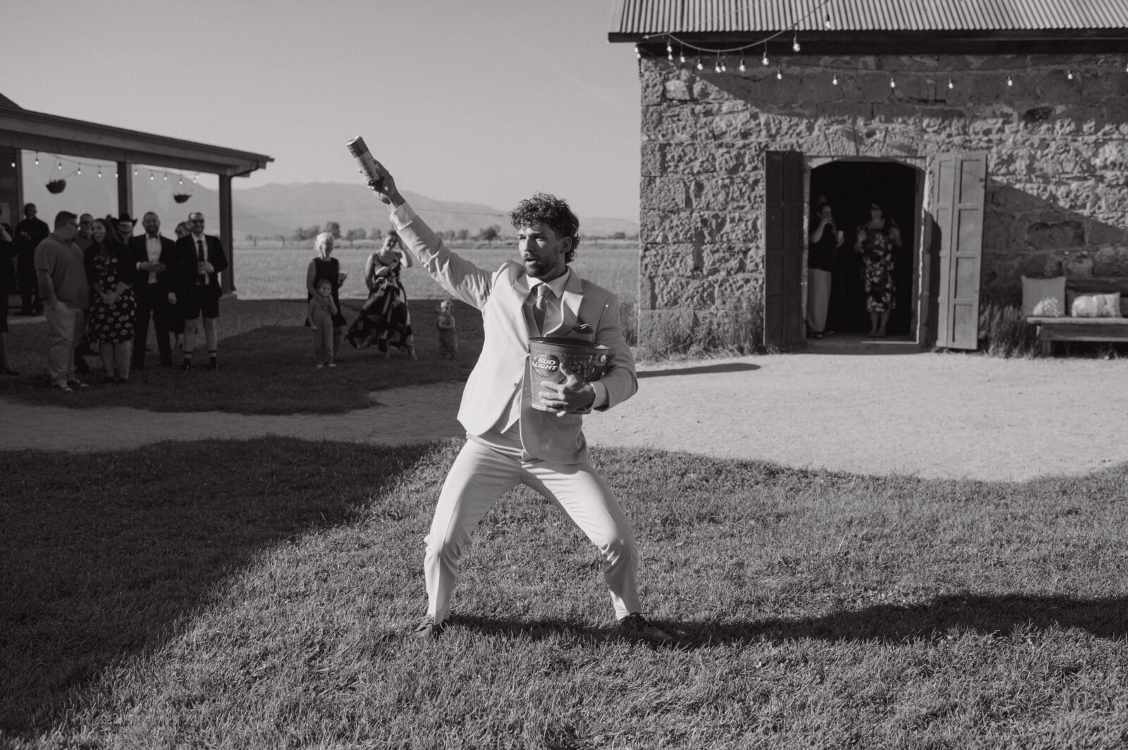 Groomsman carrying a bucket of beer across the lawn outside the stone barn during cocktail hour.