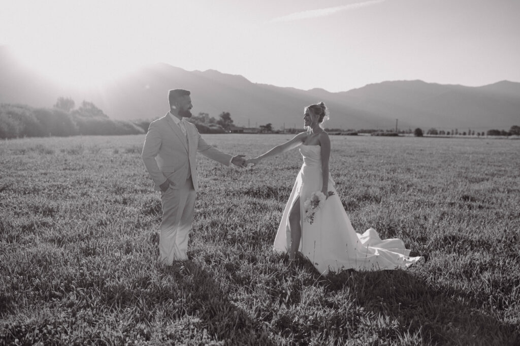 Black and white photo of a bride and groom holing hands in a field during golden hour for their Gansberg Ranch wedding.