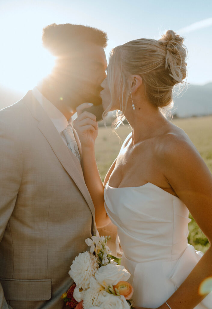 Bride and groom kissing in warm golden hour light with the sun shining behind them.