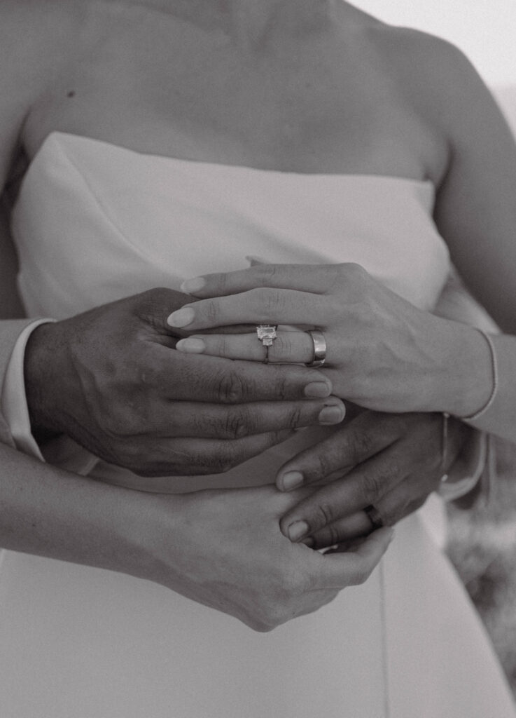 Black and white close-up of the bride and groom’s hands showing their wedding rings.