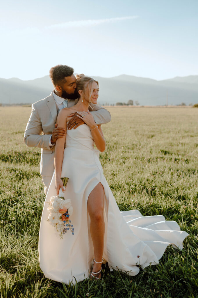 Groom hugging the bride from behind during golden hour portraits in an open field.