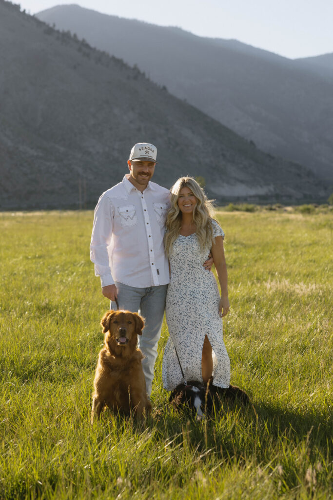 Couple smiling as they pose in front of the mountains with their two dogs.