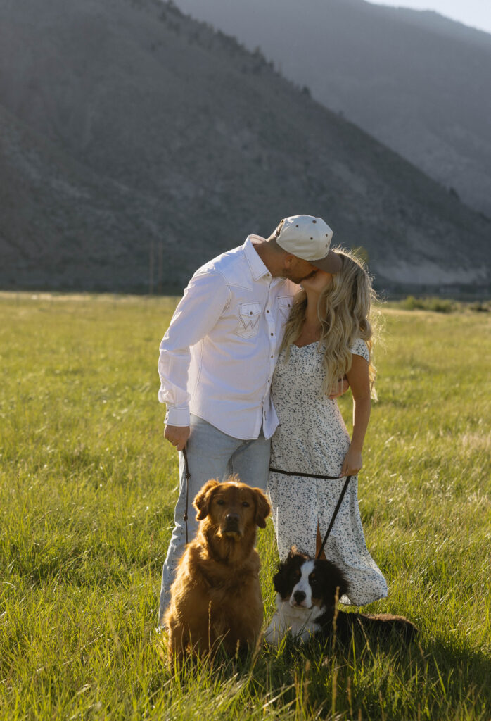 Couple kissing with their dogs sitting in front of them.