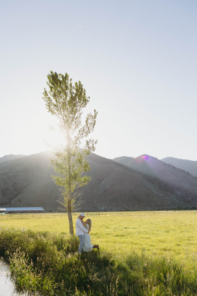 Couple posing near a tree with mountains in the background at golden hour. 