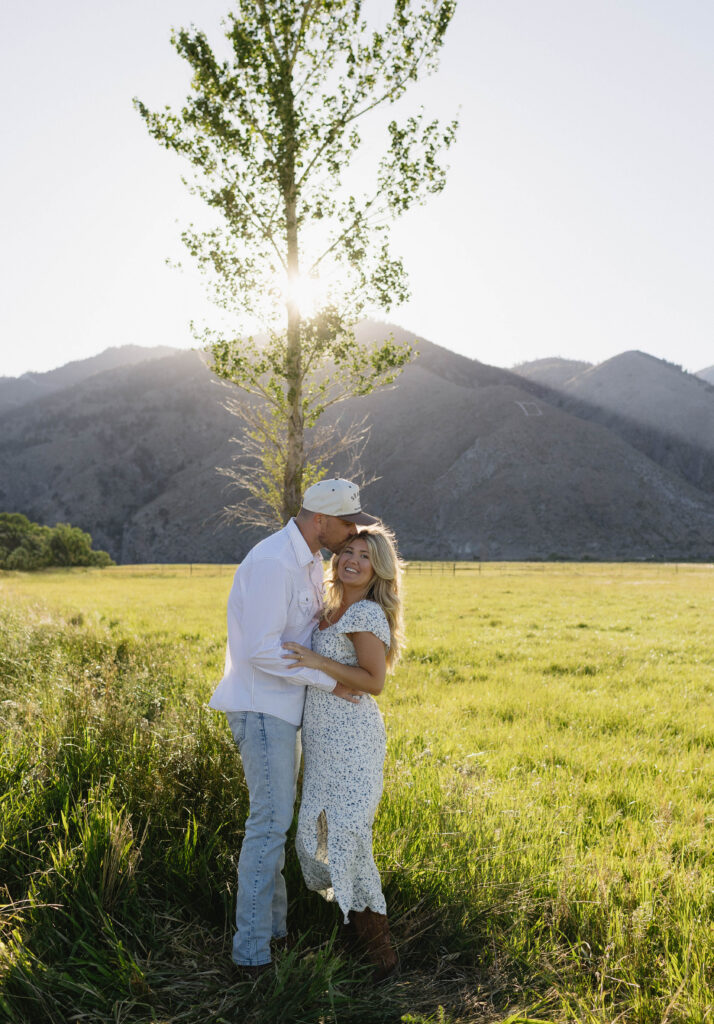 Couple posing near a tree with mountains in the background at golden hour. 