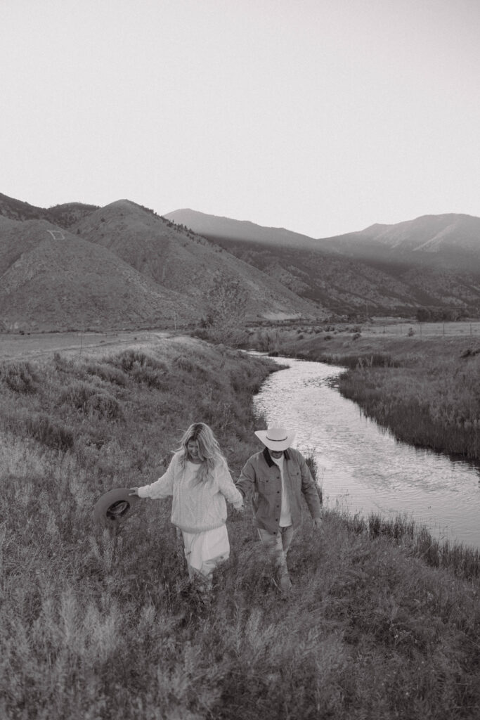 Couple holding hands and walking up a grassy hill during their mountain engagement photos in Genoa, Nevada with Jobs Peak in the background.