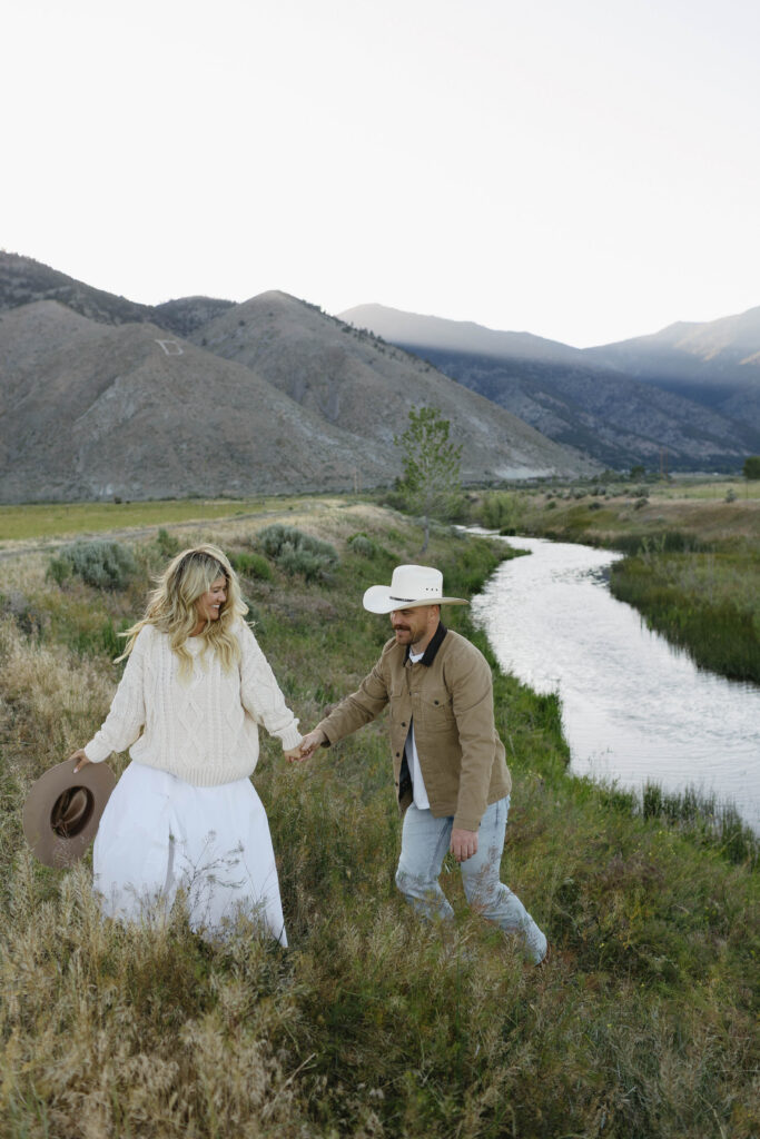 Couple walking up a hill with the river behind them and Jobs Peak in the background. 