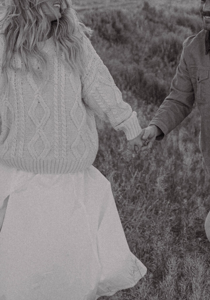 Close up film inspired shot of a couple holding hands and walking up a grassy hill.