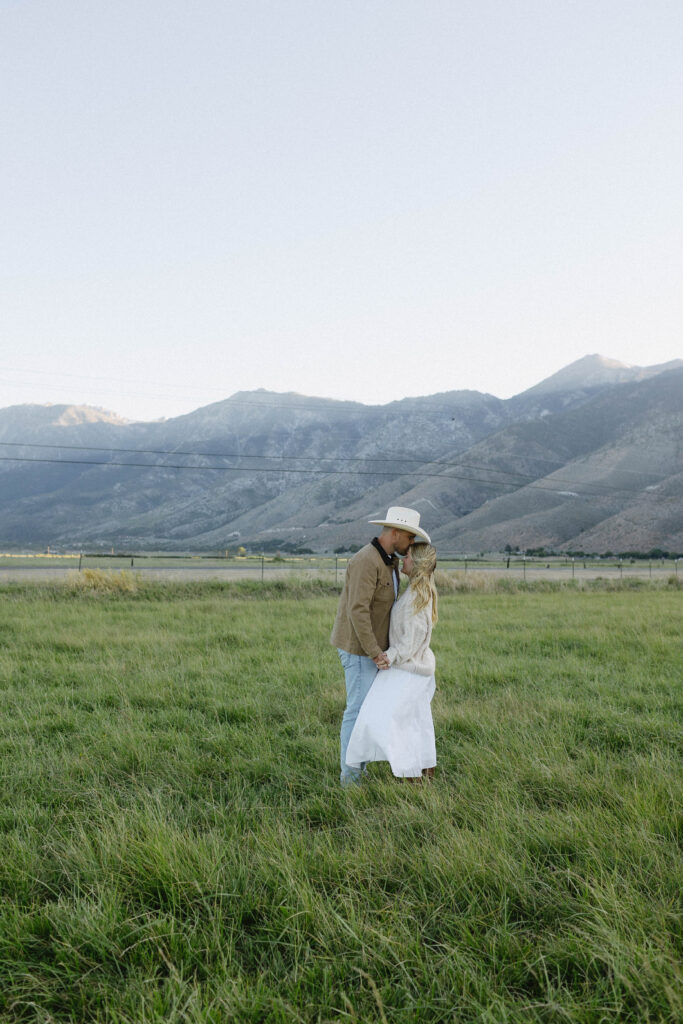 Man kissing his fiancés forehead during their mountain engagement photos with jobs Peak in the background at blue hour.