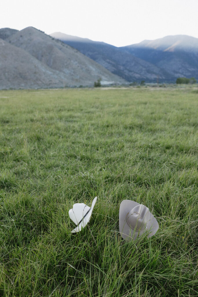Two cowboy hats laid out in the grass with Jobs Peak in the background.