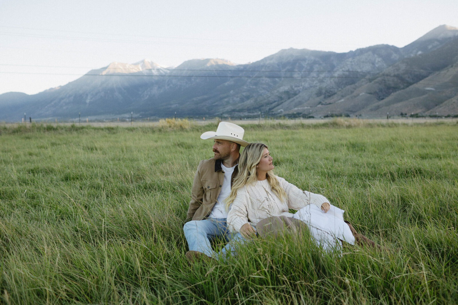 Couple sitting in an open grassy field during their blue hour engagement photos in Genoa, Nevada with Jobs Peak in the background.