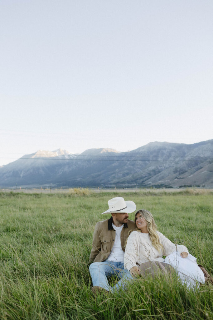 Couple sitting in the grass during their mountain engagement photos in Genoa with Jobs Peak in the background. 