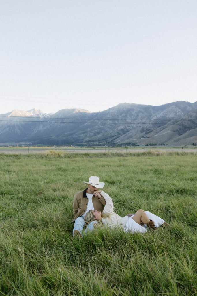 Couple sitting in the grass during their mountain engagement photos in Genoa with Jobs Peak in the background. 